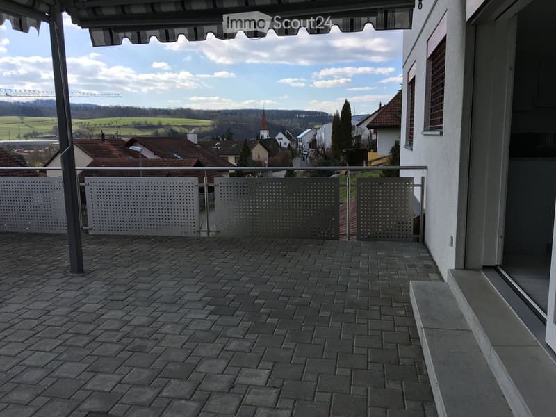 Balcony with brick tiles, metal railing, and a view of a rural landscape with houses and hills.