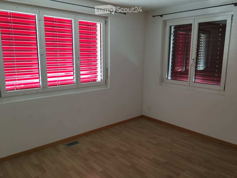 Empty room with wooden flooring, white walls, and large windows with red blinds.