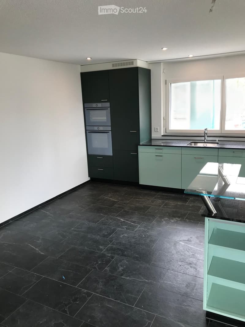 Modern kitchen with dark grey tiles, light green cabinets, stainless steel oven, and a glass countertop.