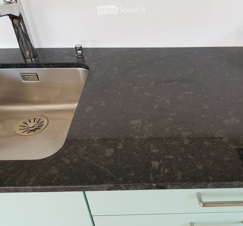 Modern kitchen sink with a sleek, dark granite countertop and a stainless steel sink, featuring a contemporary faucet and a pop-up drain stopper.