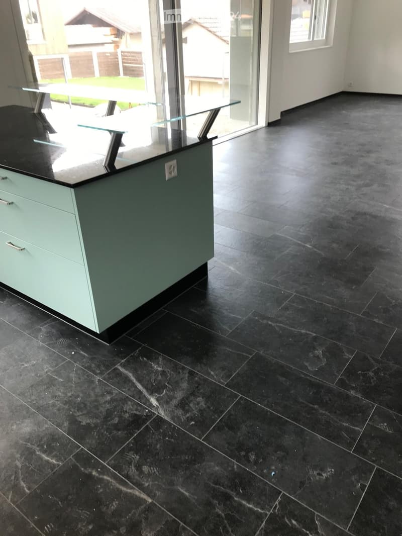 Empty room with dark tiled floor and a small island with a glass countertop and light green cabinets.