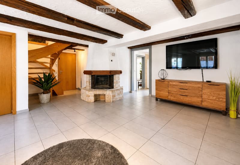 Living room with exposed wooden beams, fireplace, television, wooden cabinet, potted plants, and a rug.