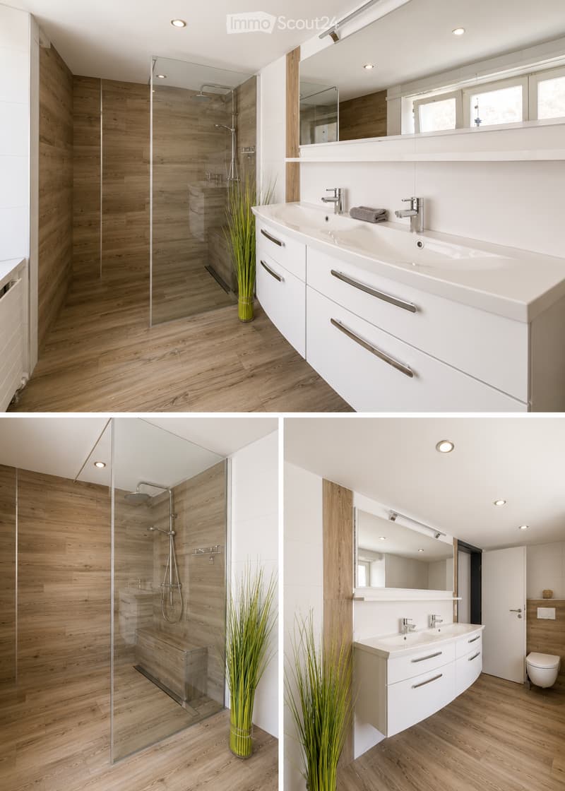 Modern bathroom with wooden flooring, white cabinetry, double sink, large mirror, glass-enclosed shower, and decorative plant in a vase.