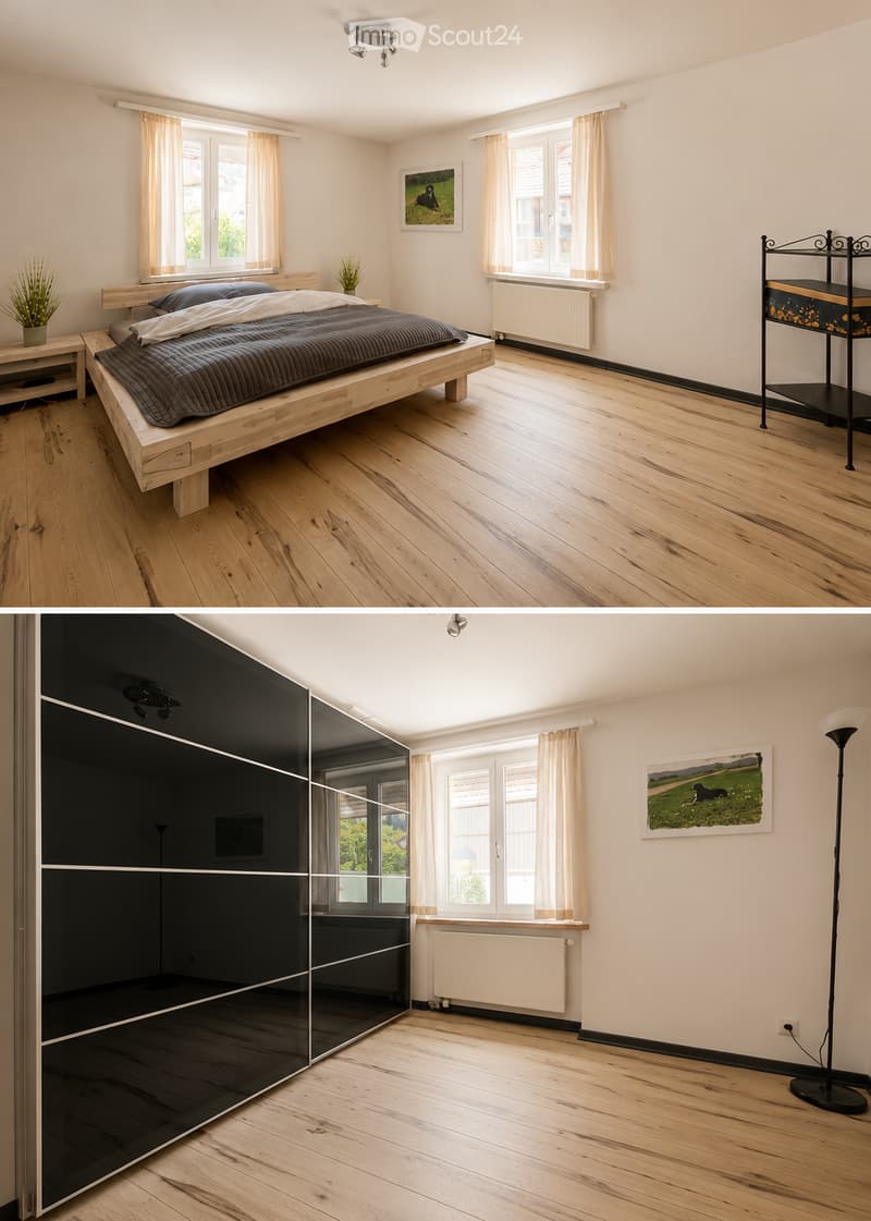 Bright bedroom with wooden flooring, large windows with curtains, a modern bed with dark bedding, a nightstand with a plant, a picture frame on the wall, and a sleek black shelving unit.
