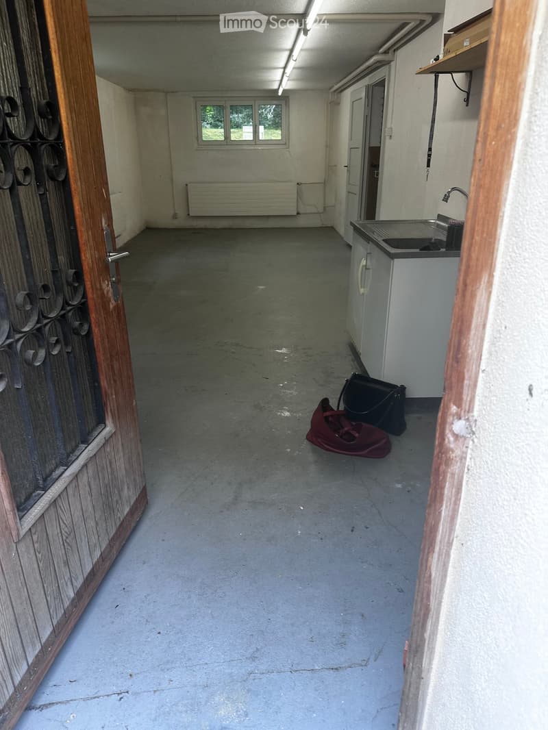 Empty hallway with concrete floor, white walls, a window, a radiator, and a small sink area with a faucet and cabinet.