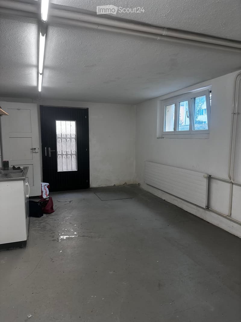 Empty room with concrete floor, white walls, a door with a glass panel, a window, and a radiator. No furniture or equipment present.