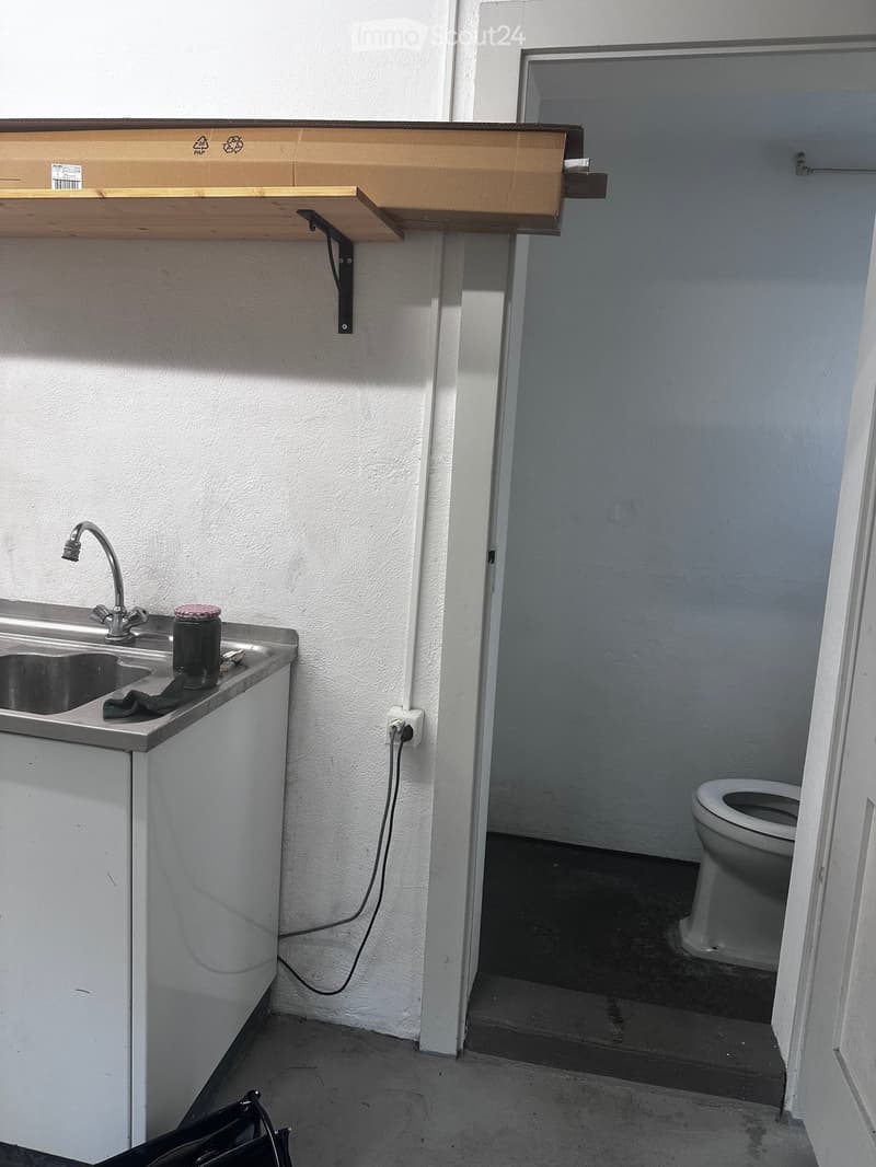 Bathroom with a sink, faucet, and a toilet in an adjacent room. A wooden shelf is mounted on the wall above the sink.