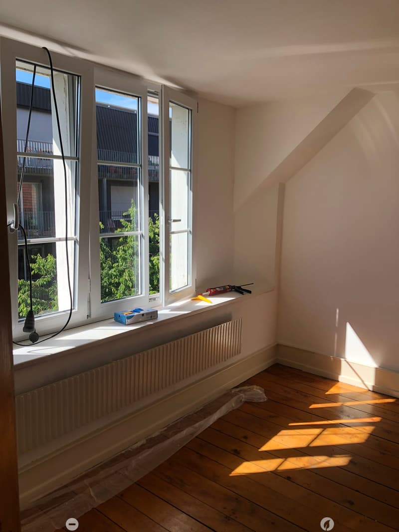 Empty room with wooden flooring, large windows, radiator, and some construction materials on the windowsill.