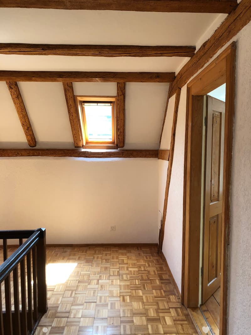 Wooden staircase with a slanted ceiling and exposed wooden beams, featuring a skylight window and a wooden door leading to another room.