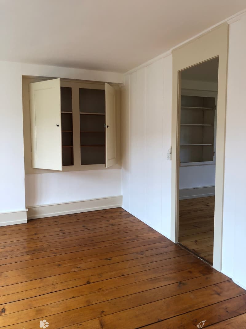 Empty room with wooden flooring, white walls, and built-in shelving units.