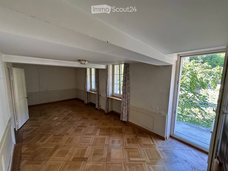 Empty room with wooden flooring, large windows, and a sliding glass door leading to a balcony or outdoor area.
