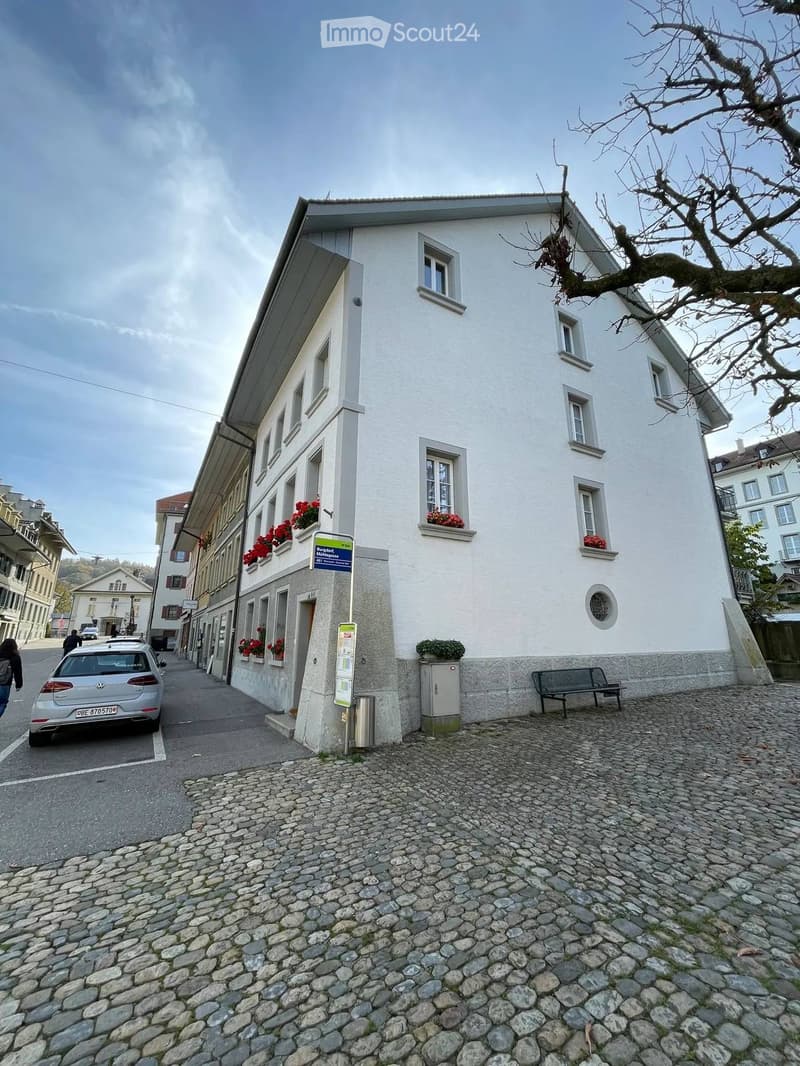 Two-story white building with multiple windows, red flower boxes, and a cobblestone sidewalk in front.