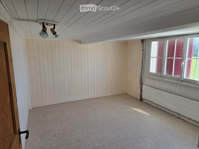 Empty room with wooden panel walls, carpeted floor, white ceiling with recessed lighting, and a window with white frame and red shutters.