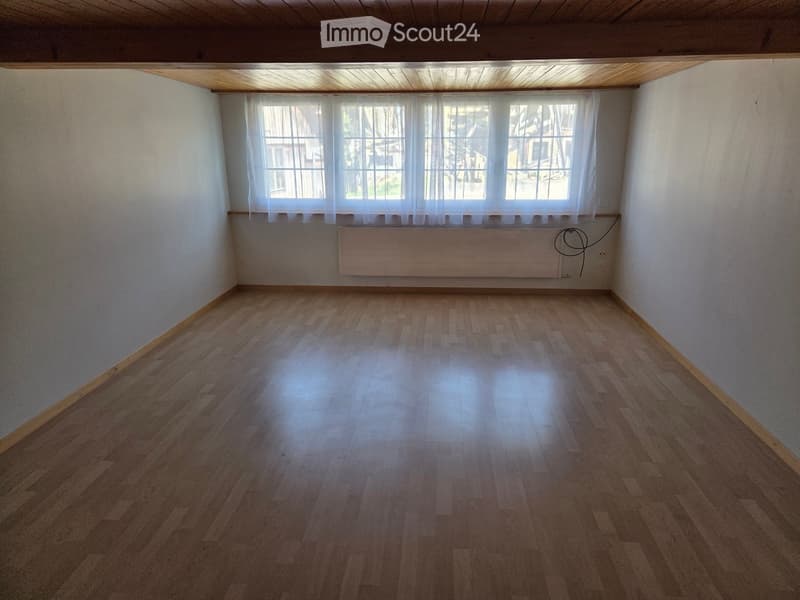 Empty room with wooden flooring, white walls, large window with white curtains, and a radiator below the window.