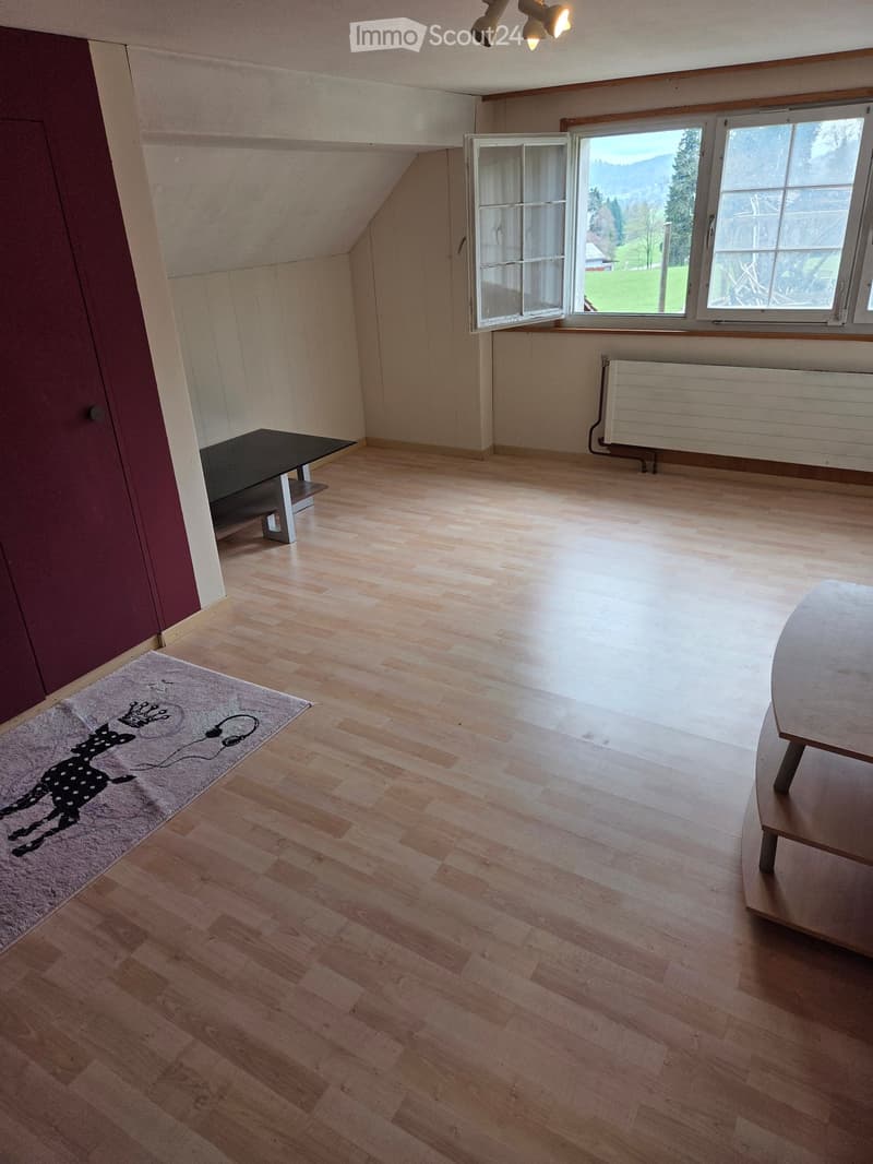 Bright, unfurnished room with wooden flooring, large windows, and a small table near the window.