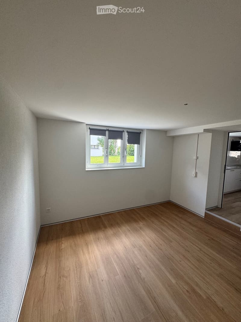Empty room with wooden flooring, light-colored walls, and a window with blinds. No furniture or equipment is present.