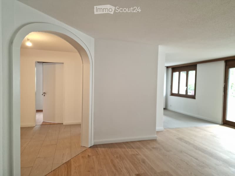 Empty hallway with wooden flooring, white walls, and an arched doorway leading to another room.