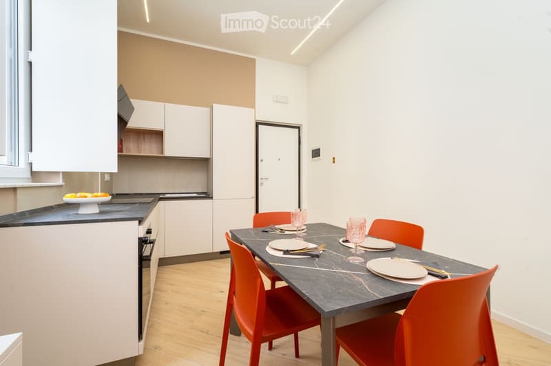 Modern kitchen and dining area with white cabinets, a black countertop, a dining table with six chairs, and a fruit bowl on the counter.