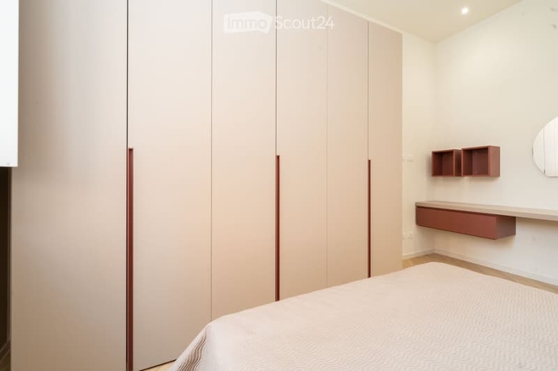 Modern bedroom with a large bed, built-in wardrobe, wall-mounted shelves, and a mirror.