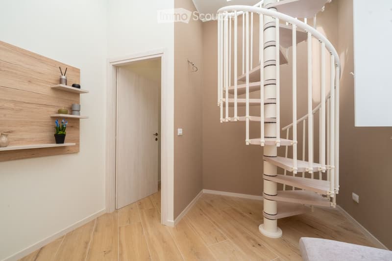 Spacious hallway with light wooden flooring, beige walls, a white spiral staircase, and a wooden shelf with decorative items.