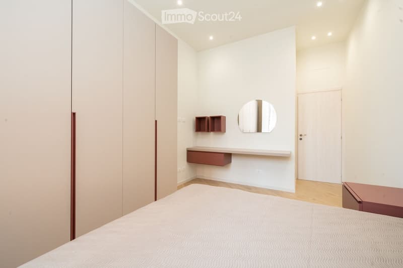 Modern, minimalist bedroom with a white bed, a round mirror, and built-in wooden shelves.
