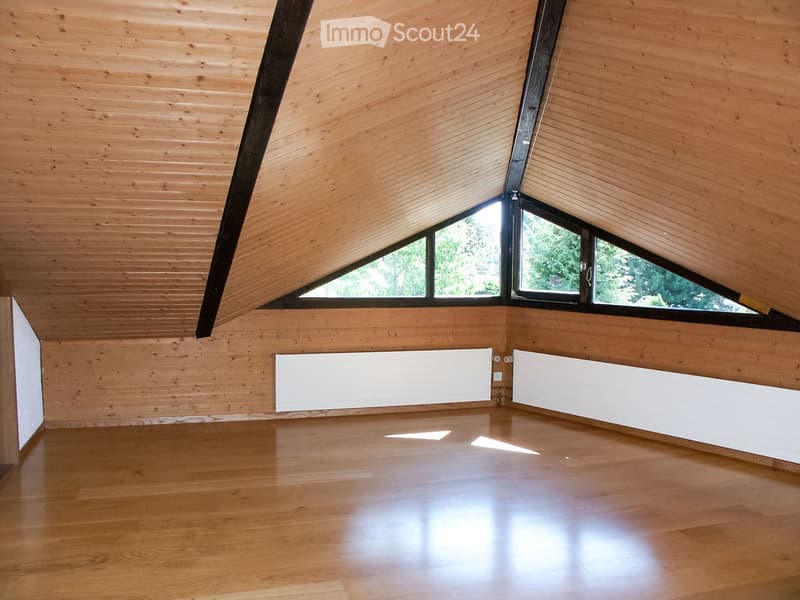 An empty room with wooden walls and ceiling, large skylight windows, and a polished wooden floor.