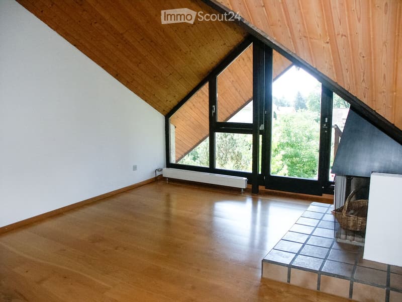 Empty room with wooden floor, white walls, large window, and fireplace area.
