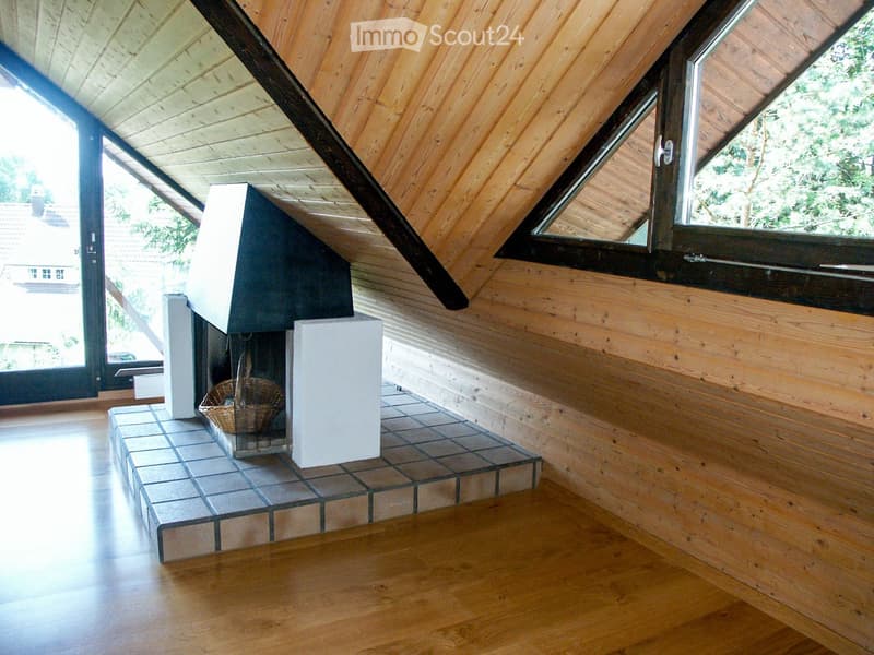 Modern living room with wooden walls and ceiling, large windows, and a central fireplace with a tiled base and a small basket on the hearth.