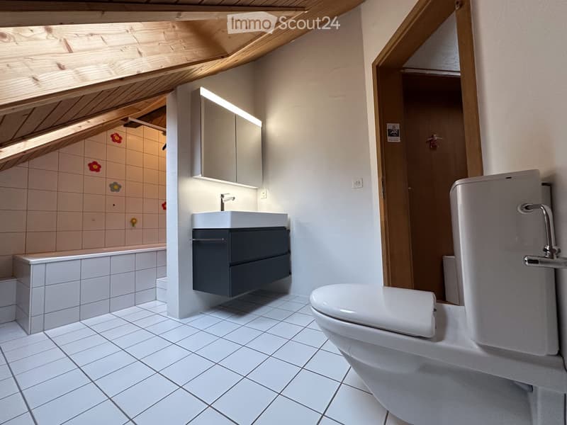 Modern bathroom with white tiles, a sink with a dark cabinet, a toilet, and a bathtub with decorative floral tiles.