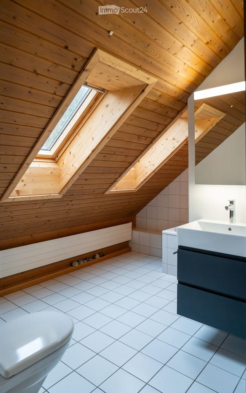 Modern attic bathroom with wooden ceiling, skylights, white tiled floor, toilet, sink, and dark cabinet.