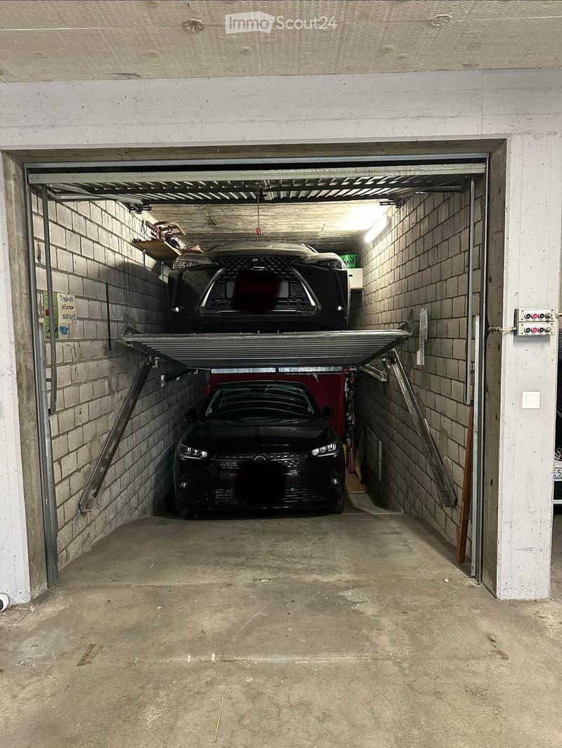 Underground garage with two cars, one parked on a lift, and exposed brick walls.