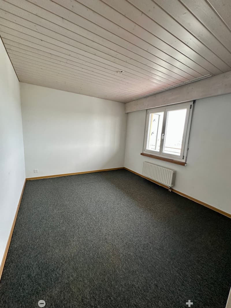 Empty room with grey carpet, white walls, wooden trim, and a window with a radiator below it.