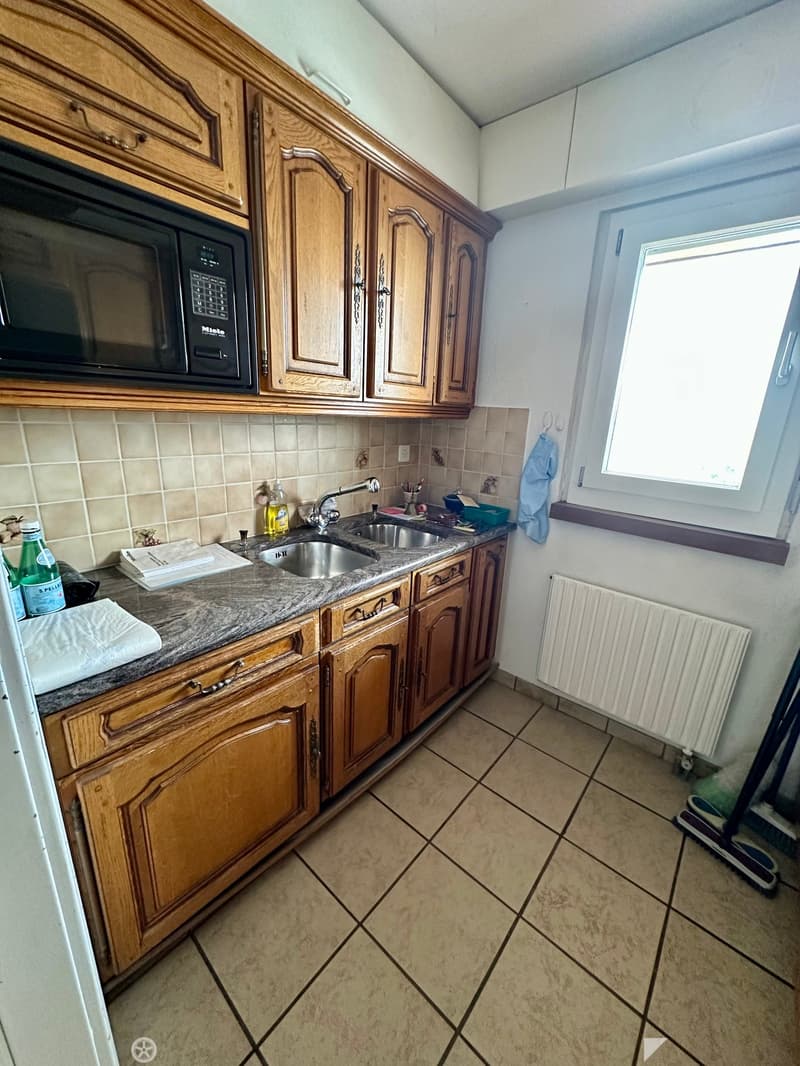 Kitchen with wooden cabinets, granite countertop, stainless steel sink, microwave, and tiled floor.