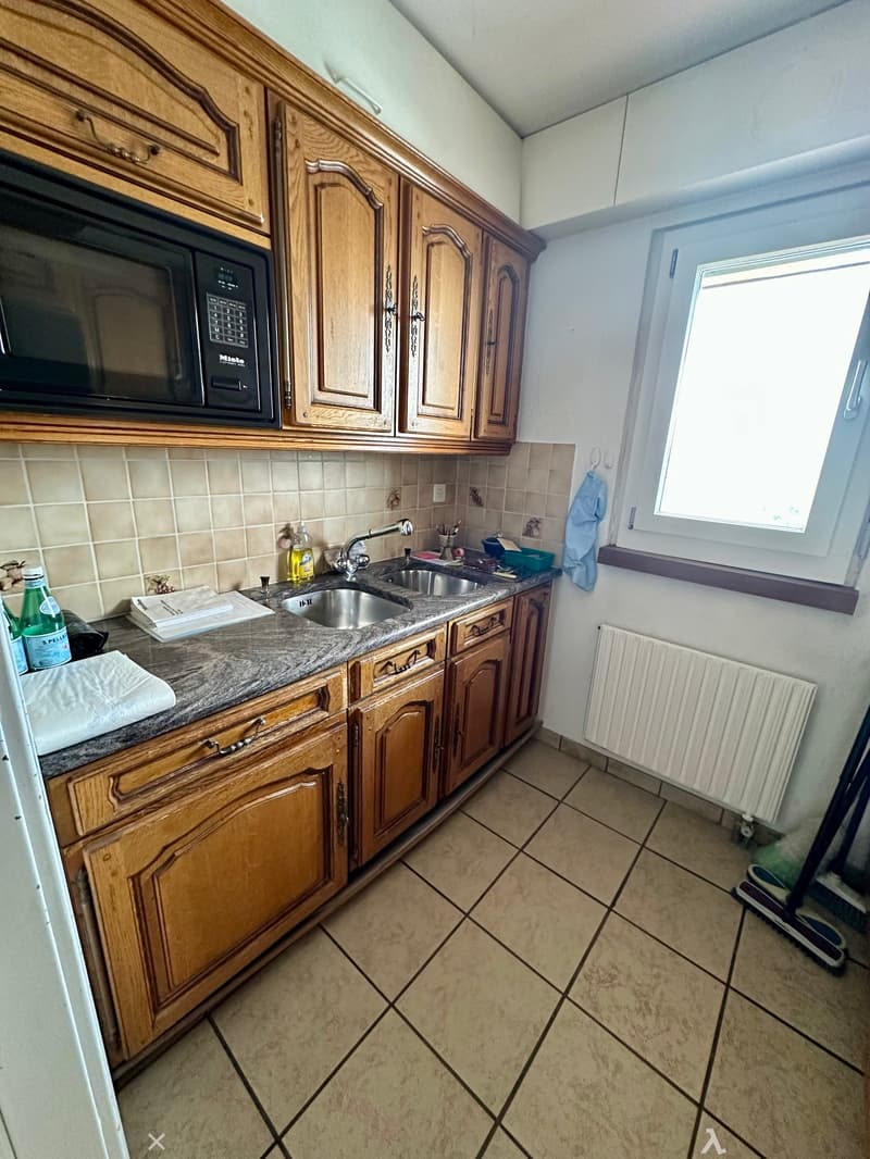 Kitchen with wooden cabinets, granite countertop, stainless steel sink, microwave, and tiled floor.