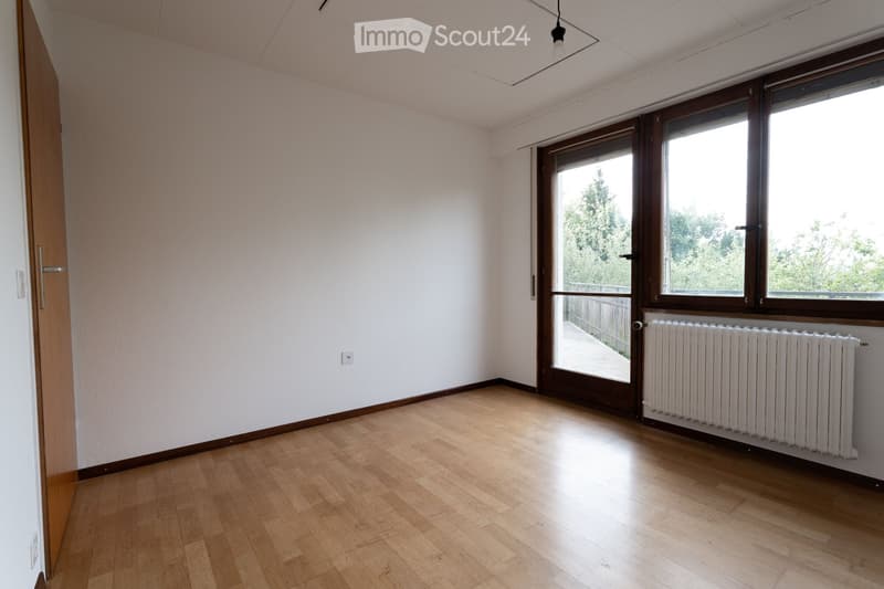 Empty room with light wooden flooring, white walls, large windows with wooden frames, and a radiator under the windows.
