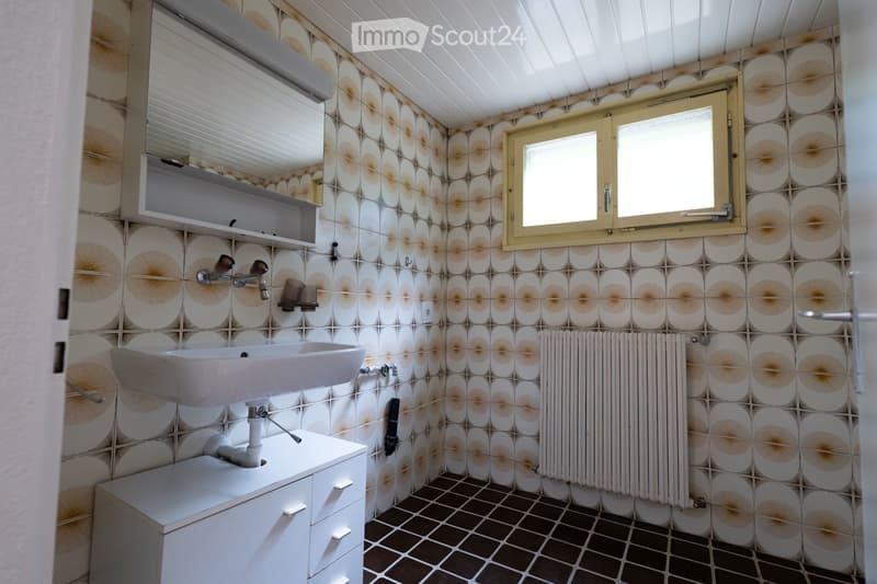 Bathroom with white sink, faucet, radiator, and cabinet. Decorative patterned tiles on walls and dark tiled floor.