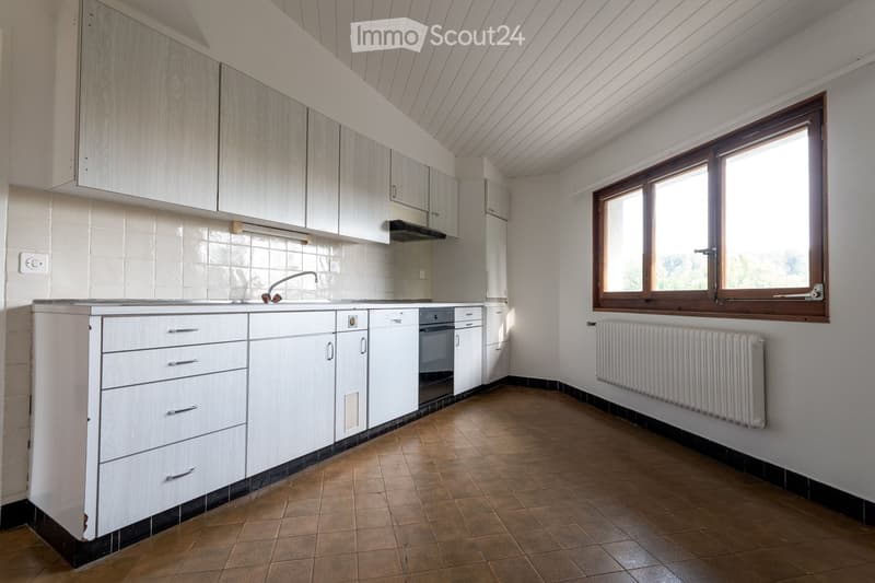 Modern kitchen with white cabinets, a sink, and a radiator under a large window.