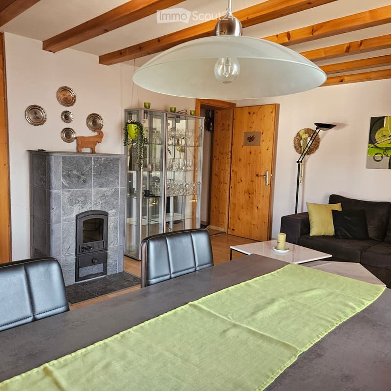 Living room with exposed wooden beams, a fireplace, a dining table with chairs, a sofa, a cabinet, and a pendant light.