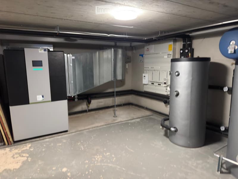Underground utility room with concrete floor, exposed pipes, electrical panels, water heater, and ventilation system.