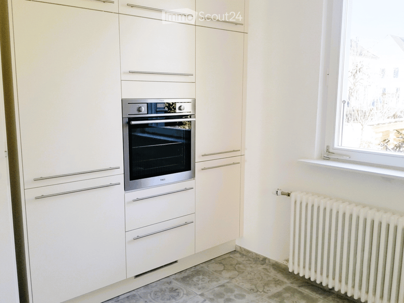 Modern kitchen with white cabinets, stainless steel oven, and a radiator under the window.
