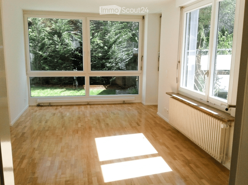 Empty room with wooden flooring, large windows, radiators, and natural light. No furniture or equipment present.