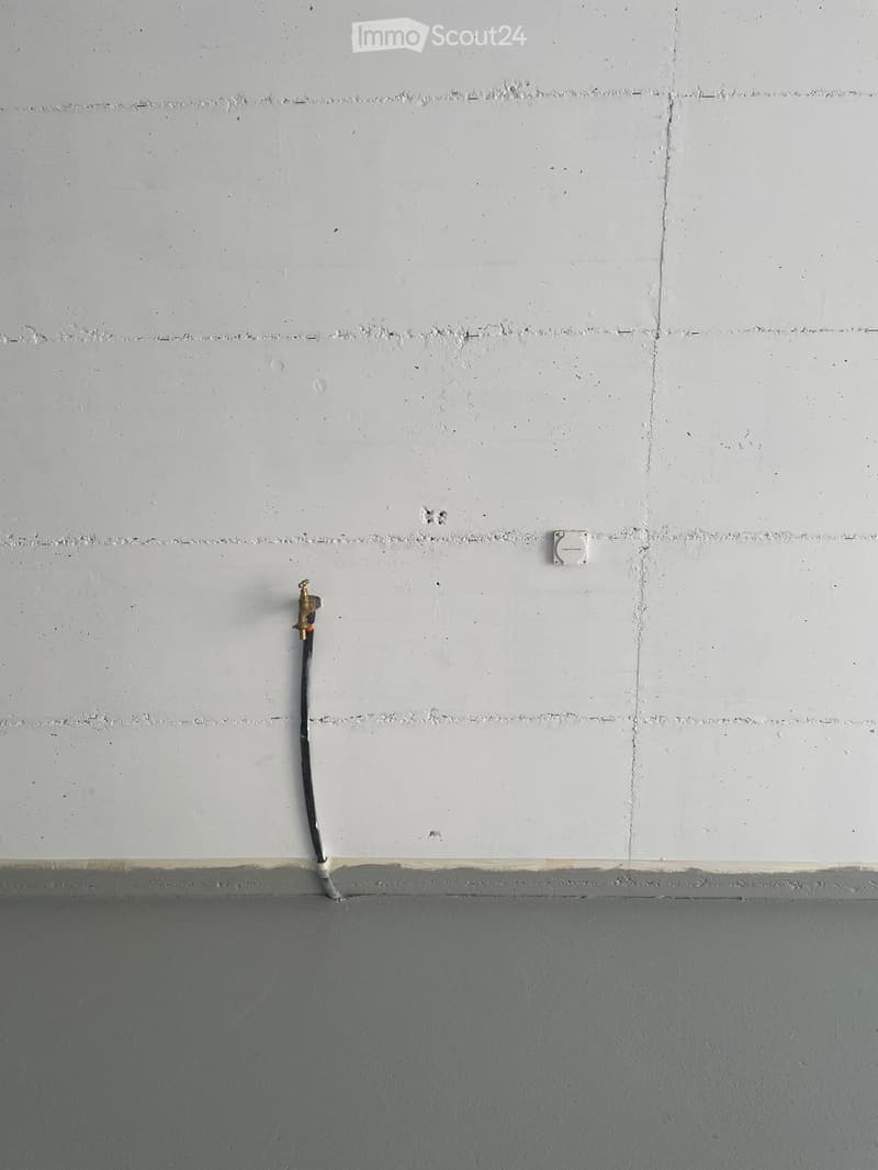 Empty room with bare walls and a floor, featuring a water tap and electrical outlet on the wall.