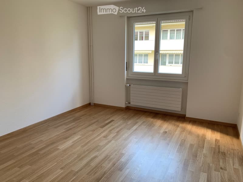 Empty room with wooden flooring, white walls, and a window with a radiator below it.
