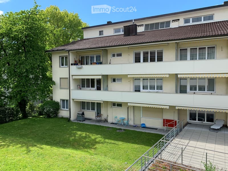 Two-story residential building with balconies, a well-maintained lawn, patio furniture, and outdoor seating area.