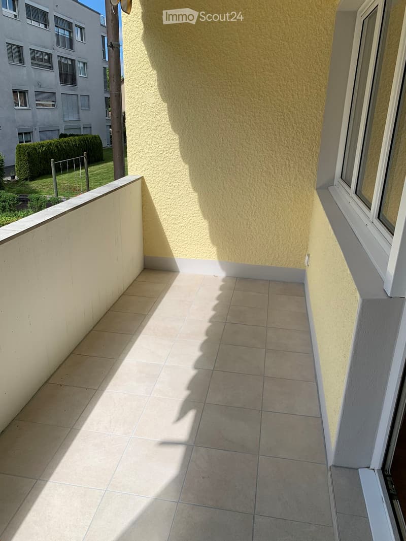 Balcony with tiled floor, white railing, and view of neighboring building and greenery.