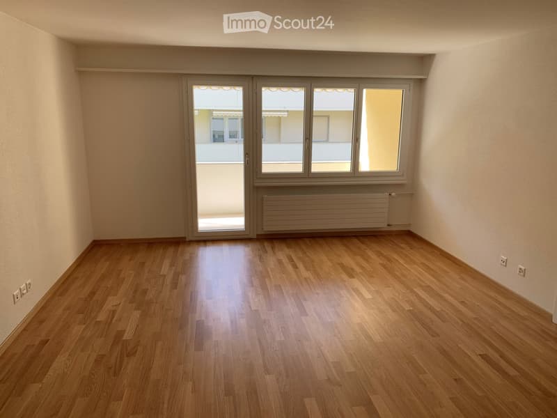 Empty room with wooden flooring, large windows, and a sliding glass door leading to a balcony.