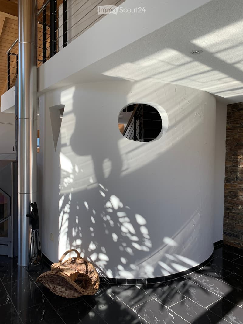 Modern hallway with white textured walls, black tiled floor, and a circular opening to another area. A wicker basket with logs is placed on the floor.