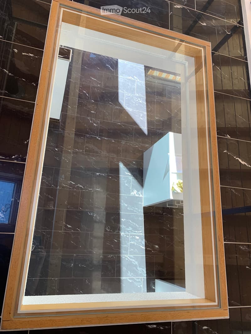 A large, framed glass display case with a marble base and wooden frame, placed in a modern interior setting.