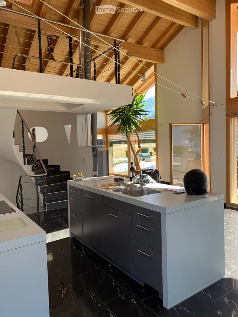 Modern kitchen with dark cabinets, white countertops, and a black marble floor. Features a sink, faucet, and various items on the counter including a helmet and a bottle.