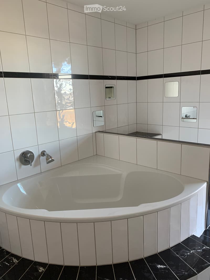 Modern bathroom with a large, curved bathtub, white tiled walls, black accents, and a sleek faucet.